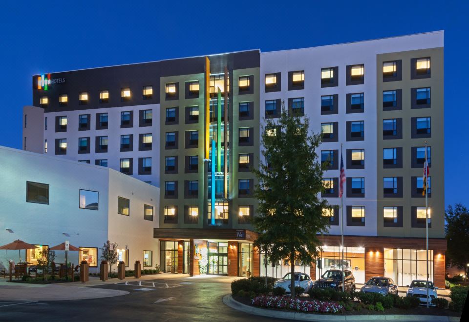a modern hotel building with multiple floors and large windows , illuminated by colorful lights at night at Even Hotel Rockville - Washington, DC Area, an IHG Hotel