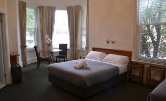 a large bed with white linens is in a room with a window and chair at Hobart Tower Motel