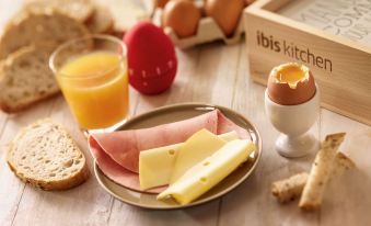 a breakfast table with a variety of food items , including eggs , bread , cheese , and a glass of orange juice at Ibis Luxembourg Sud