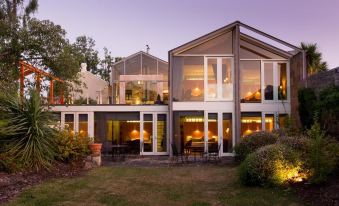 a modern house with large windows and a wooden deck is surrounded by greenery , lit up at night at Islington Hotel