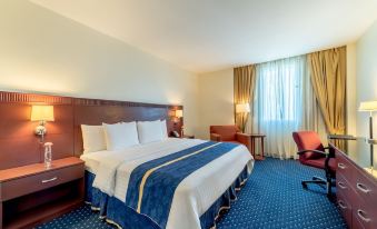 a large bed with a blue blanket is in the middle of a room with two chairs and lamps at Hodelpa Garden Court