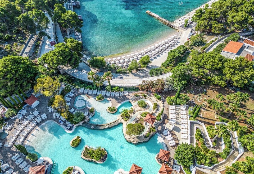 aerial view of a resort with a large pool surrounded by multiple beach chairs and umbrellas , overlooking the ocean at Amfora Hvar Grand Beach Resort