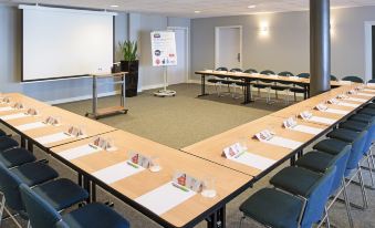 a large conference room with multiple rows of tables and chairs arranged for a meeting at Ibis Luxembourg Sud