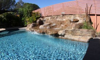 a large outdoor swimming pool surrounded by a wooden fence , with rocks scattered around the pool at Sleepy Hill Motor Inn