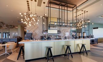 a modern coffee shop with a long counter , stools , and various coffee - making equipment , creating a cozy atmosphere at Hilton Garden Inn Doncaster Racecourse
