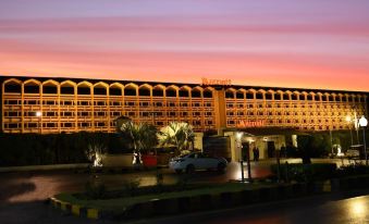a large hotel building with a parking lot in front of it , illuminated by lights during sunset at Islamabad Marriott Hotel