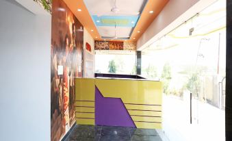 a modern office with an orange and yellow wall , a wooden reception desk , and several chairs arranged around the area at Collection O 27949 Hotel Kriti Green