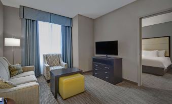 a modern living room with a large window , gray walls , and a yellow ottoman , along with a flat - screen tv on a gray cabinet at Homewood Suites by Hilton Hamilton