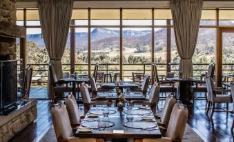 a restaurant with wooden tables and chairs , set for a meal , is situated in front of a large window at Emirates One&Only Wolgan Valley
