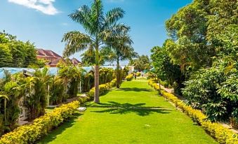 a lush green lawn with palm trees and a pathway leading to a residential area at Travellers Beach Resort