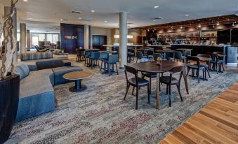 a modern lounge area with wooden tables and chairs , an overhead light , and a long bar at Courtyard Troy