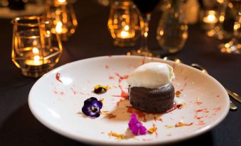 a white plate with a piece of chocolate cake on it , surrounded by candles and wine glasses at Pullman at Sydney Olympic Park