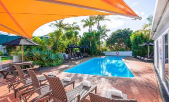 a backyard with a large swimming pool surrounded by patio furniture , including chairs and umbrellas at Scenic Hotel Bay of Islands
