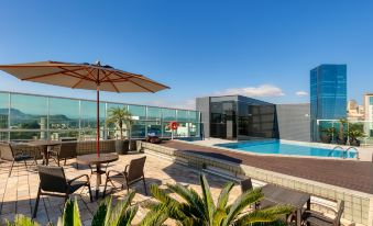 a rooftop patio with a pool surrounded by chairs and an umbrella , creating a relaxing atmosphere at Mercure Belo Horizonte Vila da Serra