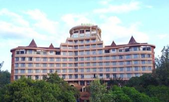 a large hotel building surrounded by trees , with a cloudy sky in the background at Rainbow Ruiru Resort