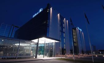 the hilton hotel lit up at night , with its name displayed in blue and white lights against a dark background at Hilton Helsinki Airport