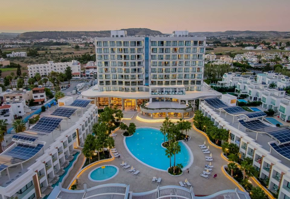a large hotel with a swimming pool and surrounding facilities , set against the backdrop of a cityscape at sunset at Radisson Beach Resort Larnaca