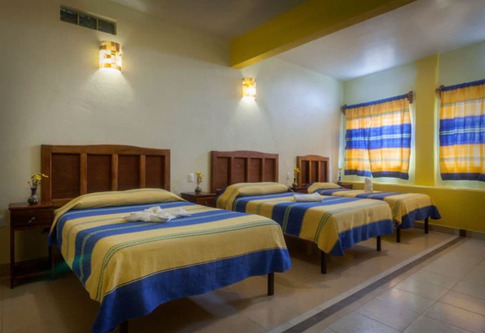 a hotel room with three beds , each made up with yellow and blue striped bedspreads , accompanied by matching curtains and wall sconces at Donaji