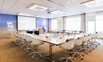 a large conference room with white chairs and a long table , set up for a meeting or presentation at Novotel Maastricht