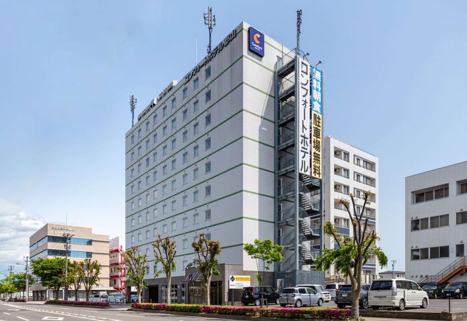a tall white building with a blue sign on the side , located in a city setting at Comfort Hotel Koriyama