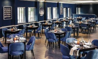 a large dining room with blue chairs and tables , creating a warm and inviting atmosphere at Mercure Swansea Hotel