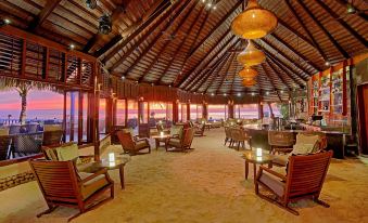 a spacious , well - lit restaurant with wooden furniture and large windows , offering a panoramic view of the ocean at Komandoo Island Resort & Spa