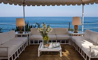 a white couch and table are set up on a patio overlooking the ocean with two lamps at Grand Hotel Baia Verde