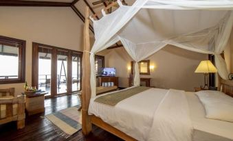 a cozy bedroom with a four - poster bed draped with a white canopy , a tv on the wall , and hardwood floors at Filitheyo Island Resort