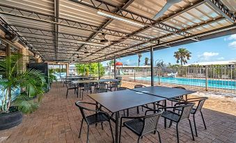 a patio area with tables and chairs set up for outdoor dining , surrounded by a swimming pool at Carnarvon Motel