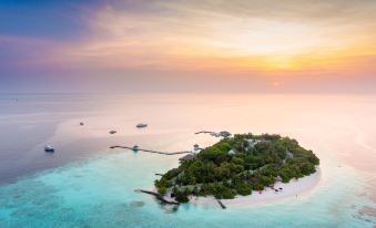 a picturesque island surrounded by clear blue water , with the sun setting behind it and boats anchored near the shore at Eriyadu Island Resort