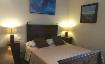a well - lit bedroom with a wooden bed , two nightstands , and a painting on the wall at Legacy