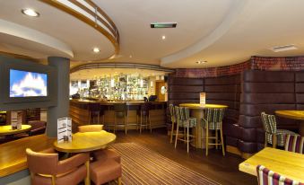 a modern bar area with wooden furniture , a curved counter , and a circular wall hanging at Premier Inn Burgess Hill
