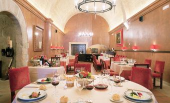 a large dining room with a round table surrounded by red chairs and a chandelier at Parador de Lerma