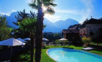 a large outdoor swimming pool surrounded by palm trees and grass , with mountains in the background at Romantik Hotel Turm