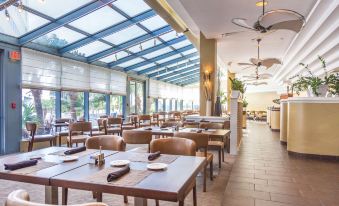 a large , well - lit restaurant with multiple dining tables and chairs , as well as a kitchen area at Hilton Melbourne, FL