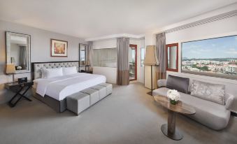 a large bed with white linens is in a room with a wooden coffee table , lamps , and potted plants at Transcorp Hilton Abuja
