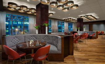 a modern restaurant with red chairs and a wooden floor , featuring curved couches , tables , and pendant lights at Hyatt Centric Arlington
