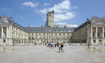 a large , open courtyard with people walking around and a tall tower in the background at Novotel Dijon Sud