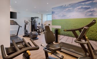 a gym with various exercise equipment , including treadmills and stationary bikes , is set up in a room with a large mural on the wall at NH Padova