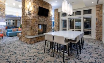a dining room with a large stone fireplace , a dining table with chairs , and a television mounted on the wall at HIlton Garden Inn Roanoke
