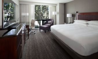a modern hotel room with a large bed , white bedding , and a view of trees outside the window at Washington Dulles Airport Marriott