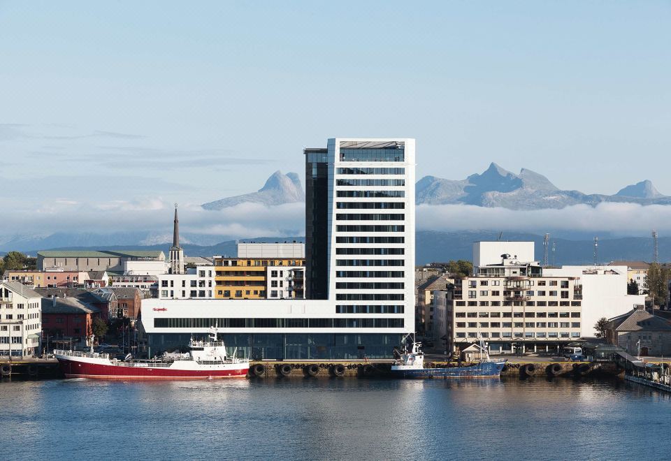 a city skyline with buildings and boats in the water , with mountains in the background at Scandic Havet