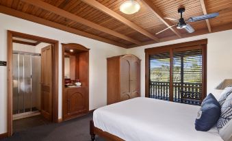 a spacious bedroom with wooden ceiling , white bedding , and a fan , along with a balcony door and wooden closet at O'Reilly's Rainforest Retreat