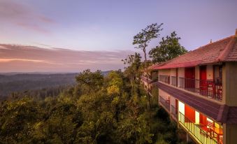 a large house with a red roof is perched on a hillside , overlooking the forest below at Coorg Cliffs Resort