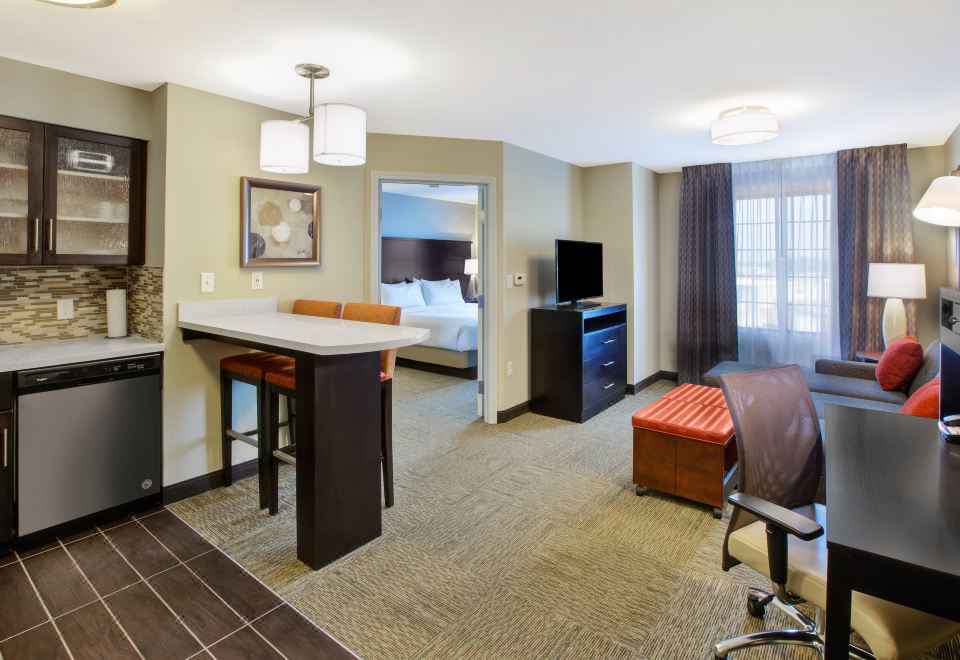 a modern living room with a dining area , kitchen , and bedroom , all connected by a small table at Staybridge Suites Benton Harbor - ST. Joseph