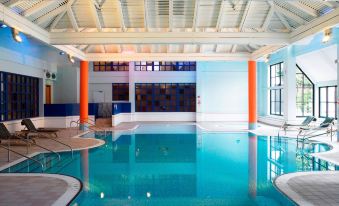 a large , empty indoor swimming pool with blue water and orange columns , surrounded by white walls and a wooden ceiling at Forest of Arden Country Club