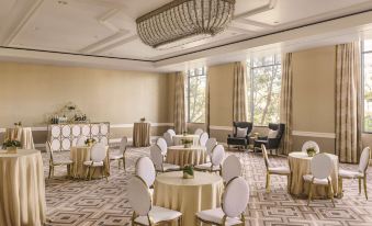 a large , well - lit room with white walls and a chandelier is filled with round tables and chairs arranged for a formal event at Signia by Hilton San Jose