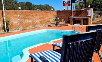a swimming pool with two blue and white striped chairs placed around it , surrounded by a brick wall at Lake Macquarie Motor Inn