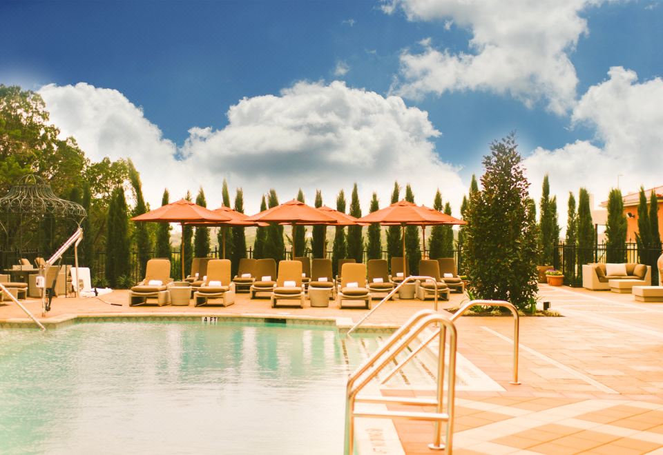 a beautiful outdoor pool area with umbrellas , sun loungers , and trees under a blue sky at Hotel Viata