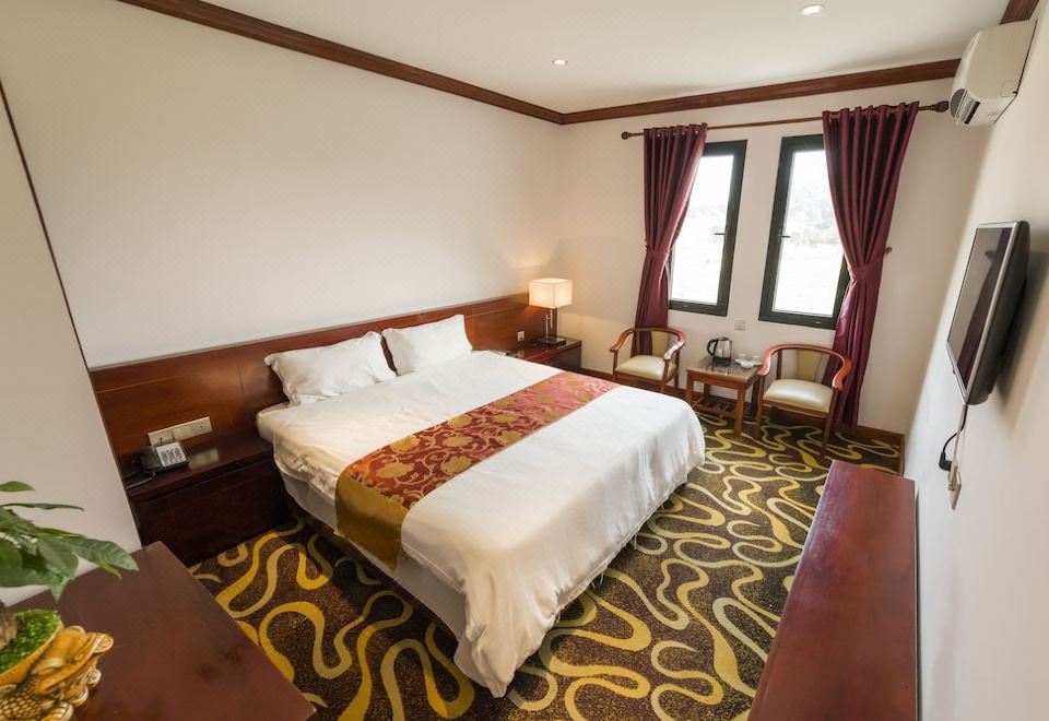 a large bed with white linens and a red and gold blanket is in the middle of a room with two windows at Hoang Trung Co to Hotel